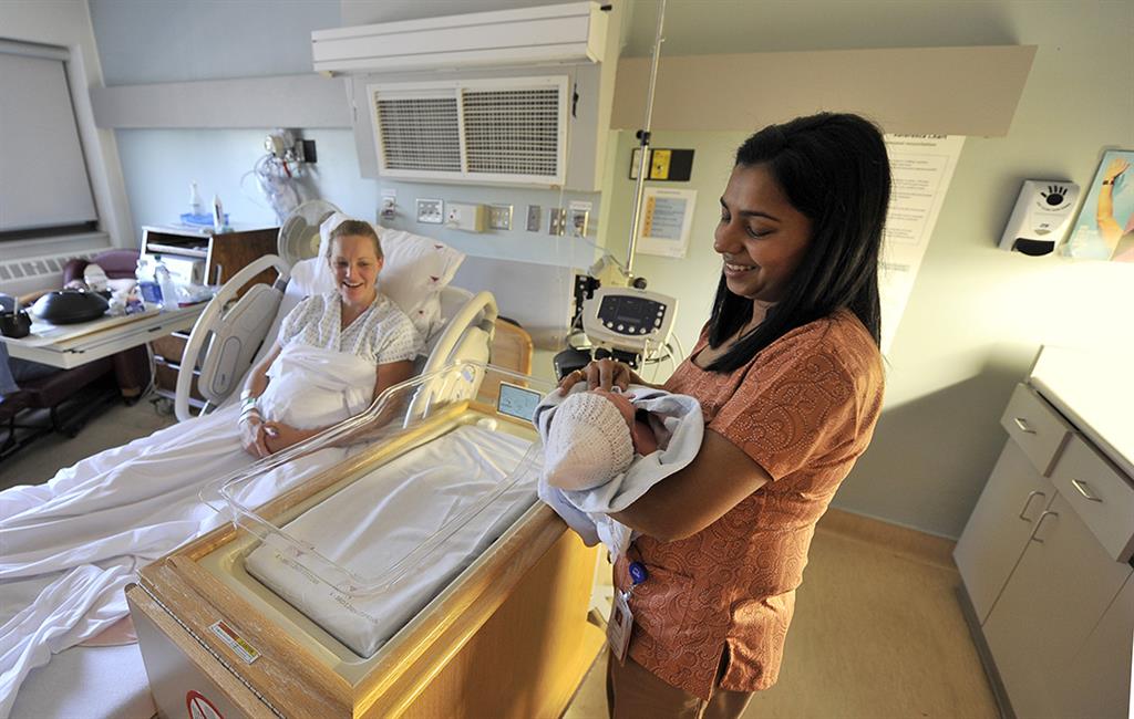 Woman in a hospital bed after giving birth, and doctor holding baby